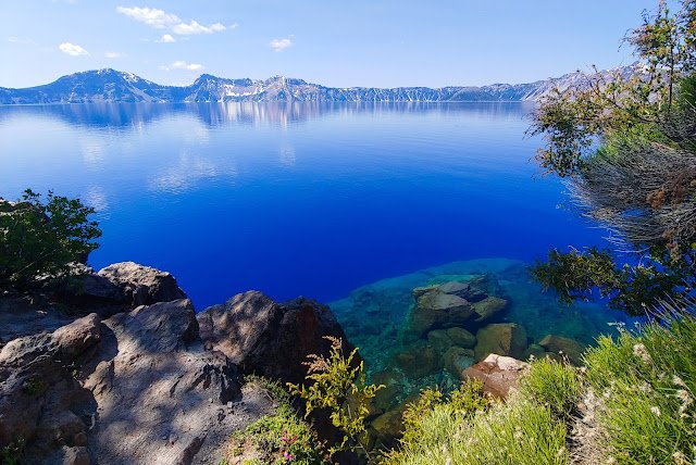 Crater Lake Surface, Crater Lake National Park Beautiful crystal blue lake with lush brush in the foreground and mountainous edge of the lake on the horizon