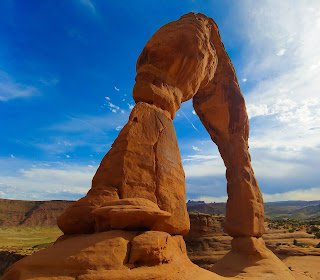 Delicate Arch, Arches National Park Large, natural rock arch against a blue sky with soft, brush stroke clouds