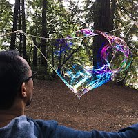 Close up of a man producing a large, elongated soap bubble using sticks and string