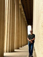 The writer of this article stands against the exterior wall of the full-sized replica of the Parthenon adjacent to a line of grand columns extending from the foreground of the image and continuing into the background