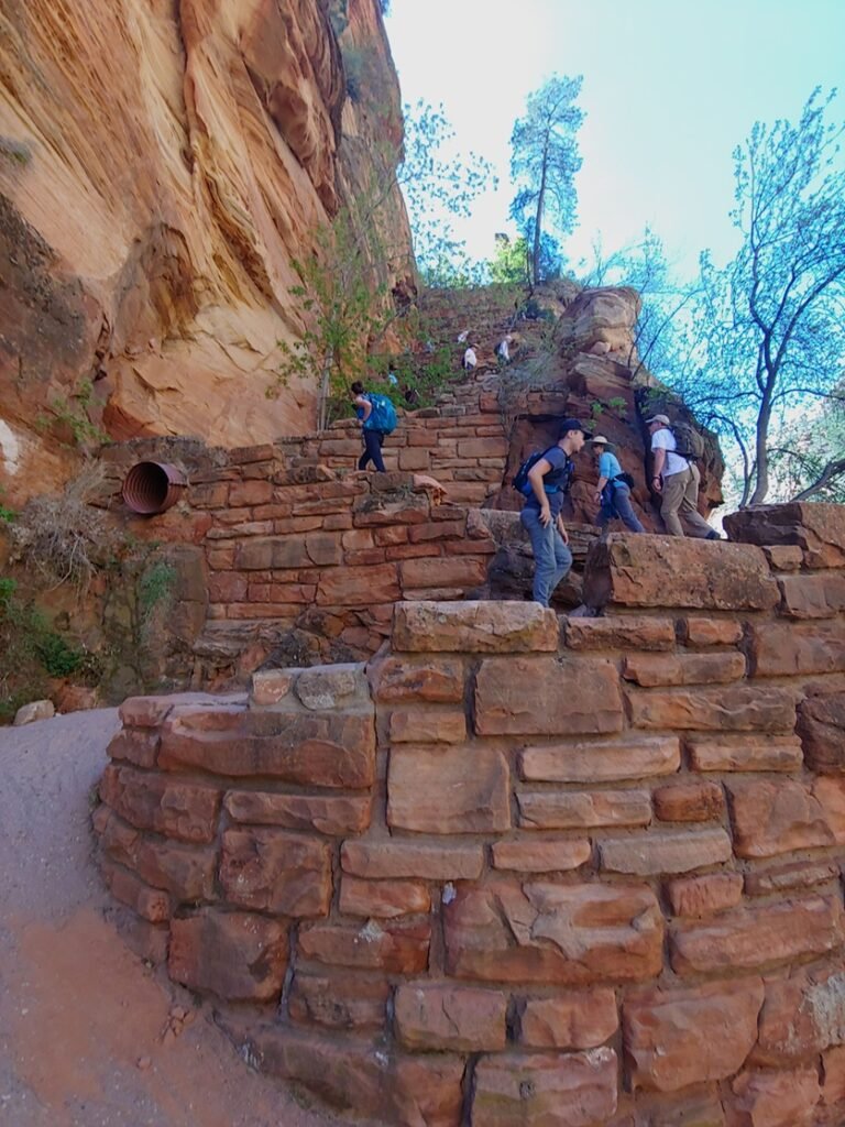 Hikers climbing a steep hill with multiple switchbacks and a gravel path supported by crafted rock retaining walls